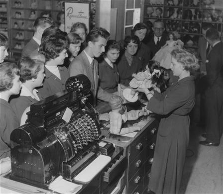 Lektion i NK-skolan. Försäljning av dockor. I förgrunden en stor kassaapparat.