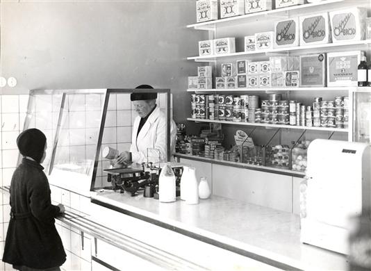 Butiksinteriör, mjölkbutik. En kund (en flicka) väntar medan mjölk hälls upp.