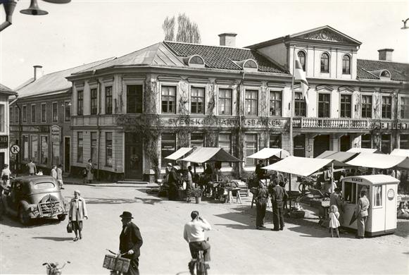 Exteriör av bankhuset och torget med torghandel.